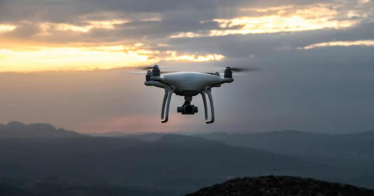 夕暮れの山岳地帯を飛行する白いドローン