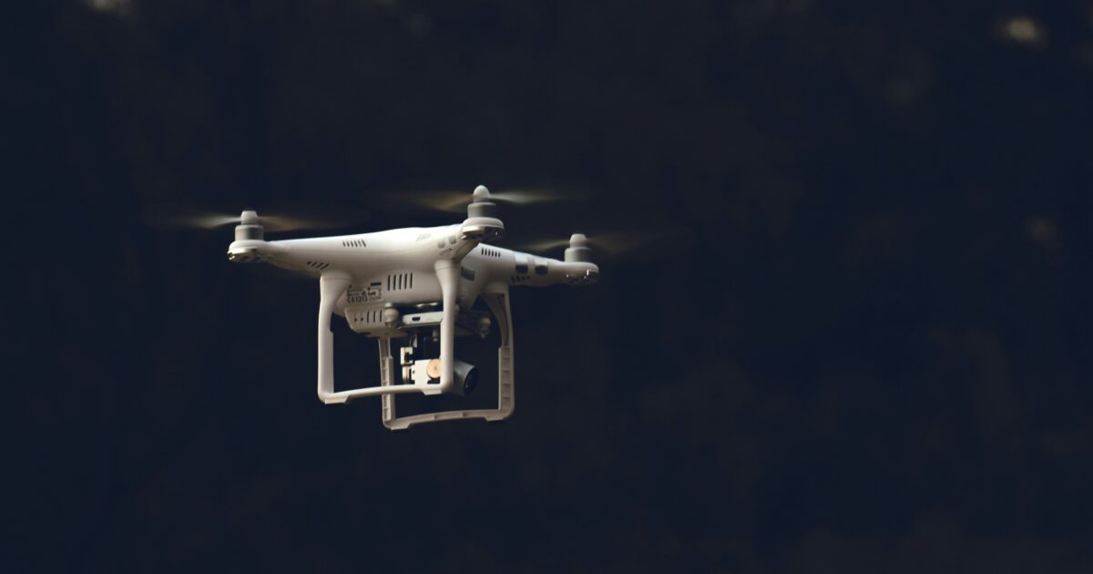 暗い背景をバックに浮かぶ白いドローン