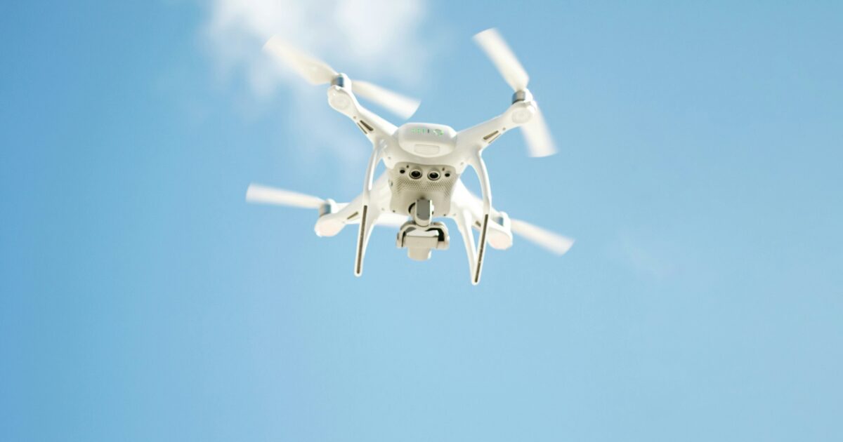 青空を背景にホバリングする白いドローン